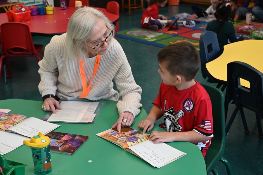 Senior volunteer helping child read at school