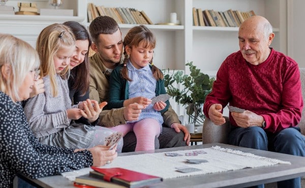 Family members are helping their aging senior members engage in a game of cards to encourage well-being and avoid feeling lonely and isolated.