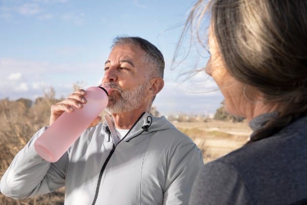 Seniors drinking water or other juices while outside walking or exercising to avoid dehydration and stay hydrated.