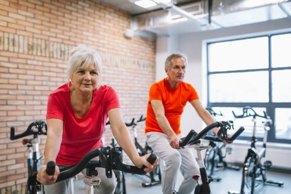 A Senior couple is using indoor bikes to exercise and strengthen their muscles and help with posture and balance.